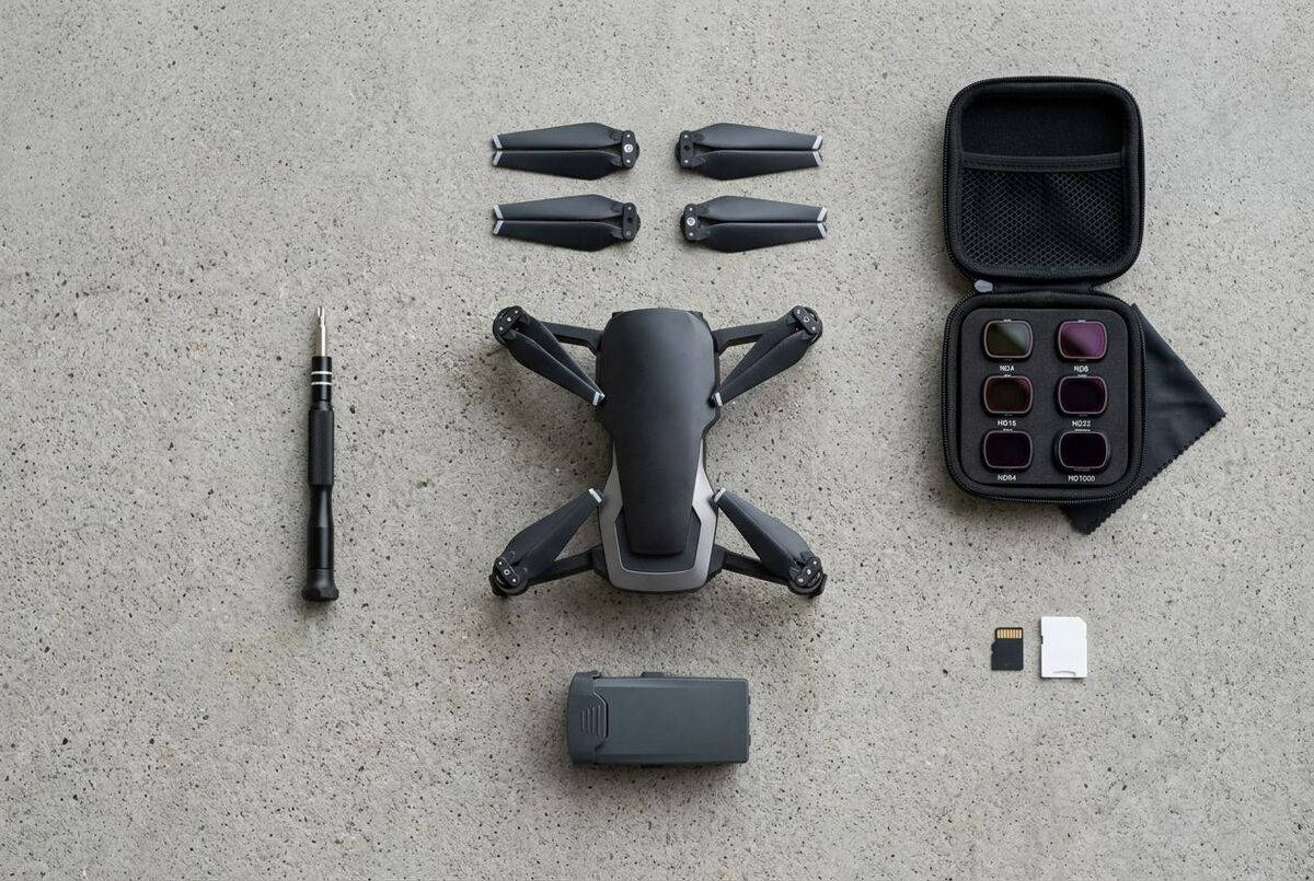 Overhead flat-lay of DJI drone with spare batteries, ND filters, SD cards and screwdriver on grey concrete surface