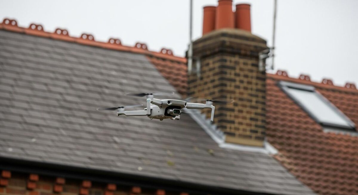 A small DJI drone flying above a tiled UK semi-detached roof