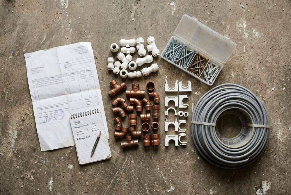 Flat-lay of plumbing fittings, electrical cable and fixings alongside a delivery note