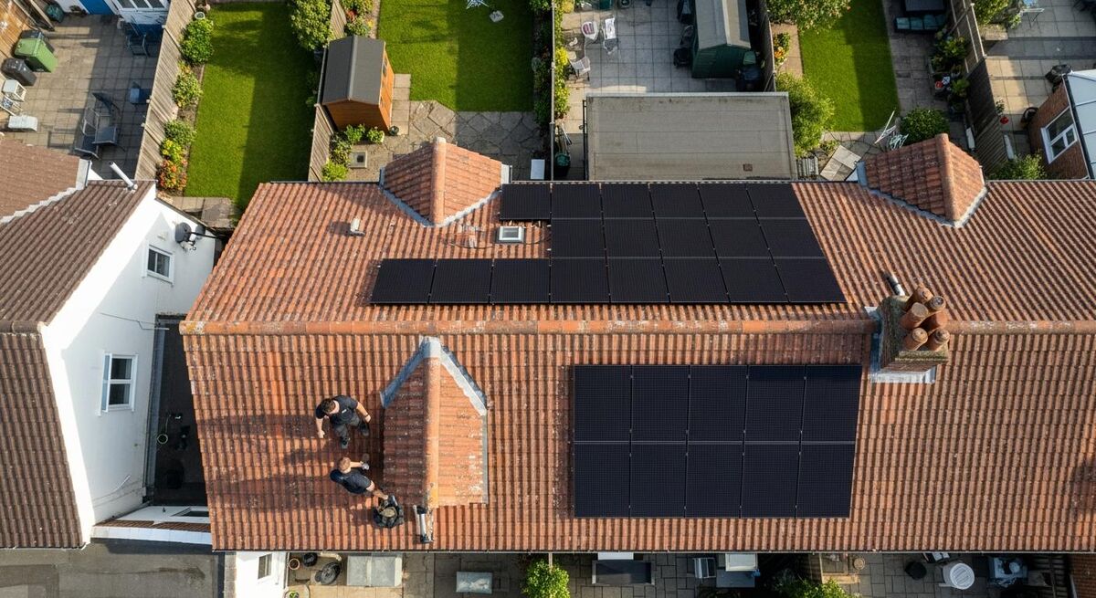 Two installers fitting solar PV panels to a residential rooftop in the UK