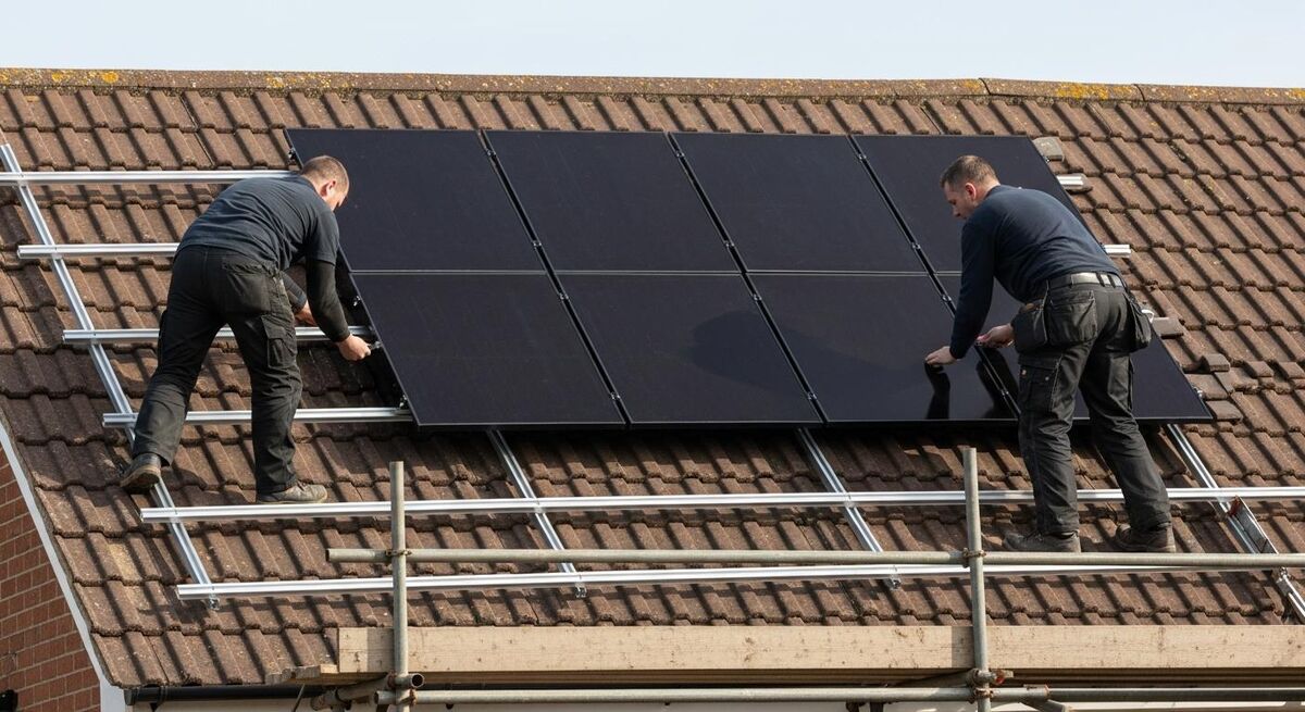 Two installers fitting solar panels on a UK pitched roof on a bright day