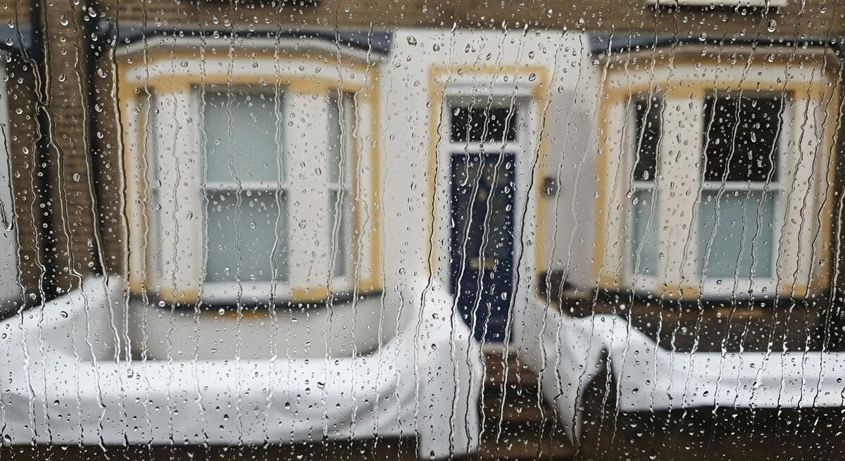 Rain droplets running down a window with a half-finished British residential exterior wall and dust sheets blurred behind
