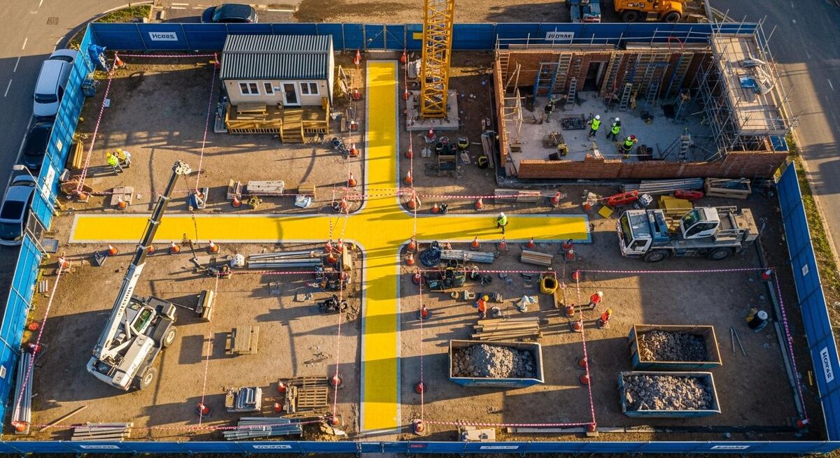 An aerial overhead view of a busy partially-built construction site with clearly marked traffic routes, plant exclusion zones, and segregated work areas.